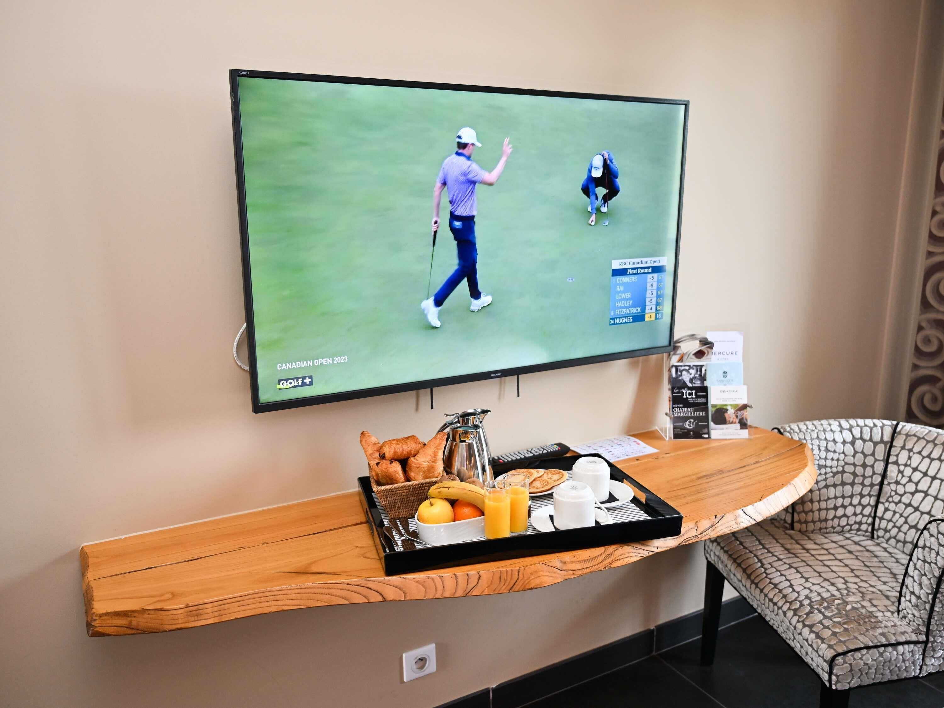Een televisie waarop een golfwedstrijd wordt getoond, een dienblad met ontbijtartikelen en een gestreept stoel.