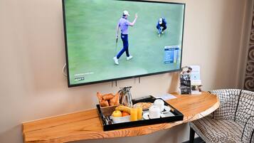 Un televisor mostrando un partido de golf, una bandeja con alimentos para el desayuno y una silla con estampado.