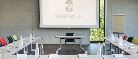 Une salle de conférence dotée d’un grand écran affichant le logo du « Barbaroux Golf Club ». On y trouve plusieurs tables, des chaises, des bouteilles d’eau et des plaques nominatives.