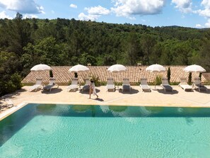 A poolside area with sun loungers and umbrellas, surrounded by a forested hillside.