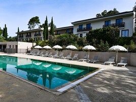 Una piscina con sillones de descanso y sombrillas, rodeada de edificios y vegetación.