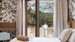 A hotel room with a bed, two towels, a nightstand, a table with chairs, and a view of the outdoors.
