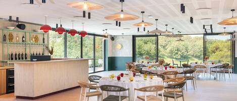 A restaurant with a bar area, round tables, and wicker chairs.