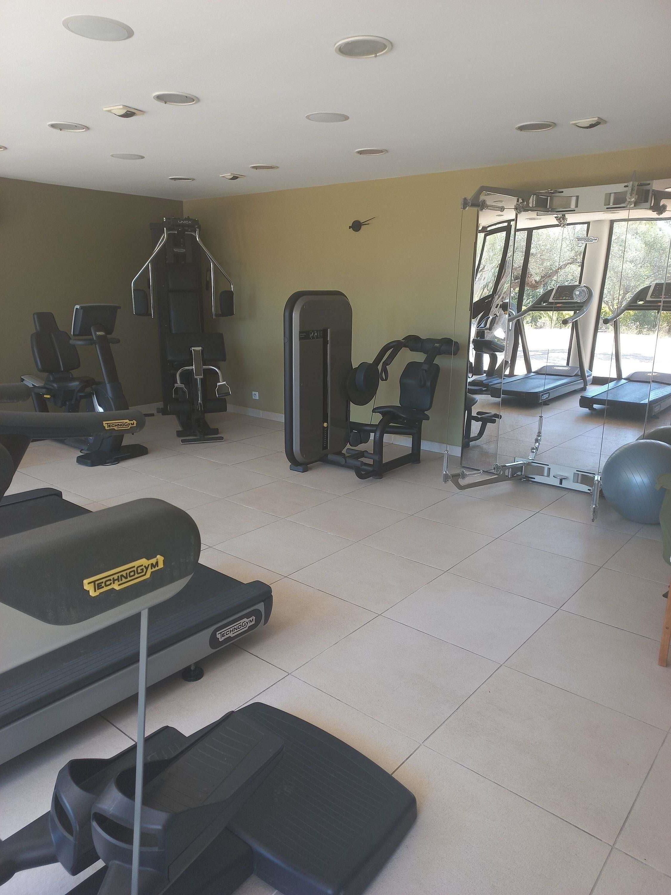 Et fitnesscenter med forskellig træningsudstyr, herunder løbebånd, et vægttræningsmaskine og en romaskine.