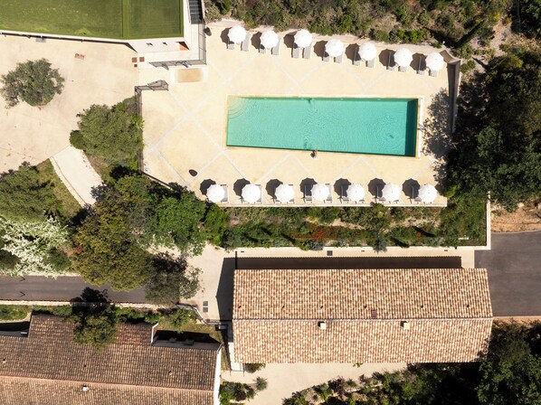 An aerial view of a resort with a swimming pool, sun loungers, and a tiled roof.