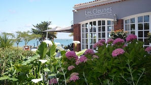 Hotel 'Les Cleunes' met uitzicht op zee, terras en weelderige begroeiing.