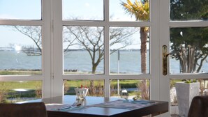 Een kamer met uitzicht op zee door een groot raam, een tafel met placemat en een deur met hendel.