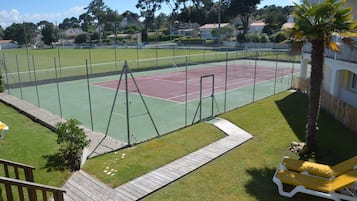 Una cancha de tenis con una red, rodeada por una cerca y una palmera.