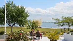 Een terras met twee personen aan een tafel, met uitzicht op een strand en de zee.