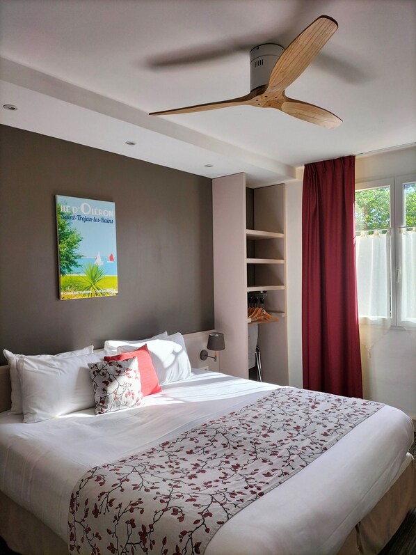 Habitación de hotel con cama, ventilador de techo, un cuadro, armario y ventana con cortinas.
