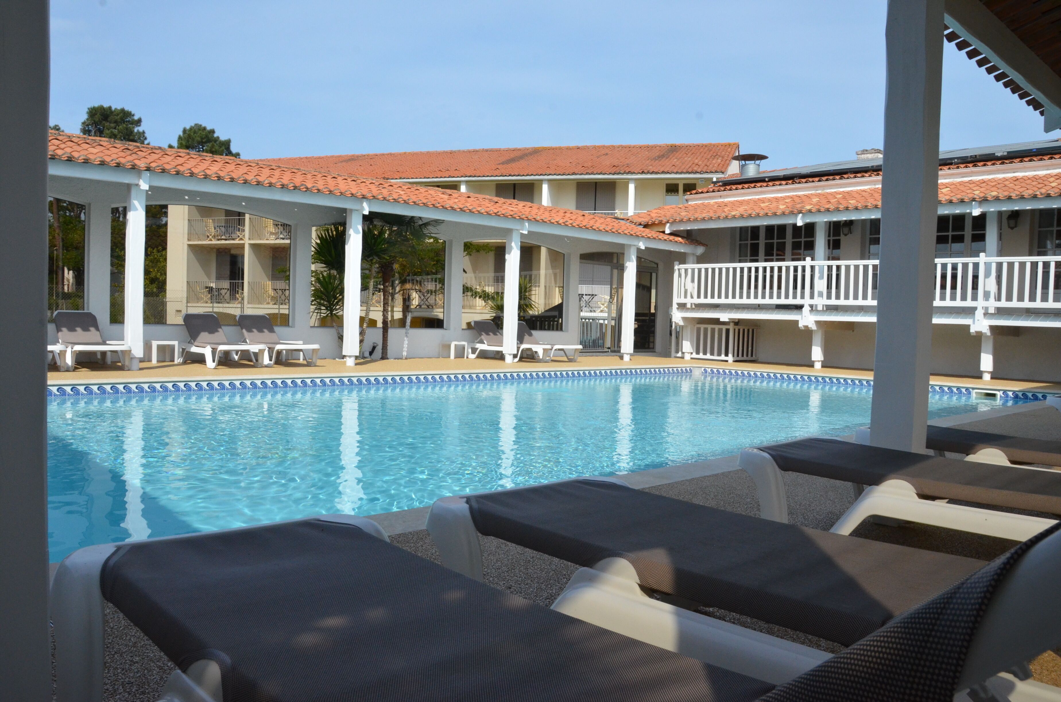 A pool area with lounge chairs and a building with a tiled roof.