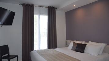 Habitación de hotel con cama, una silla, un televisor de pantalla plana en la pared y una ventana con cortinas.