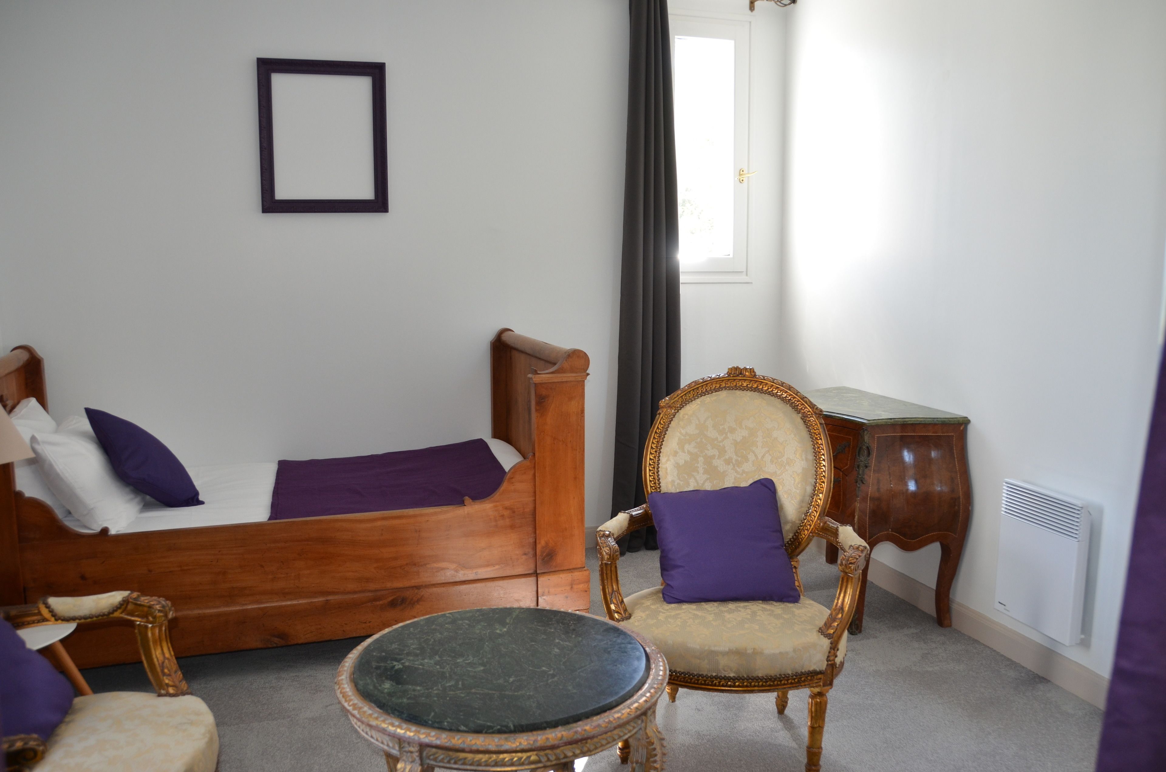 A bedroom with a wooden bed, a chair, a small table, and a radiator.