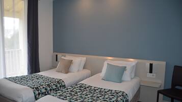 A hotel room with two beds, a window with curtains, and a nightstand with a lamp.