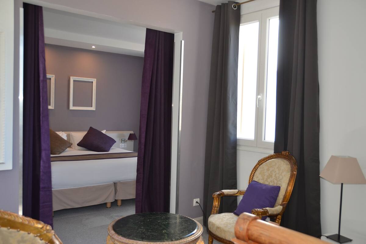 Ein Schlafzimmer mit einem Bett, einem Sessel, einer Lampe und einem Fenster mit Vorhängen.
