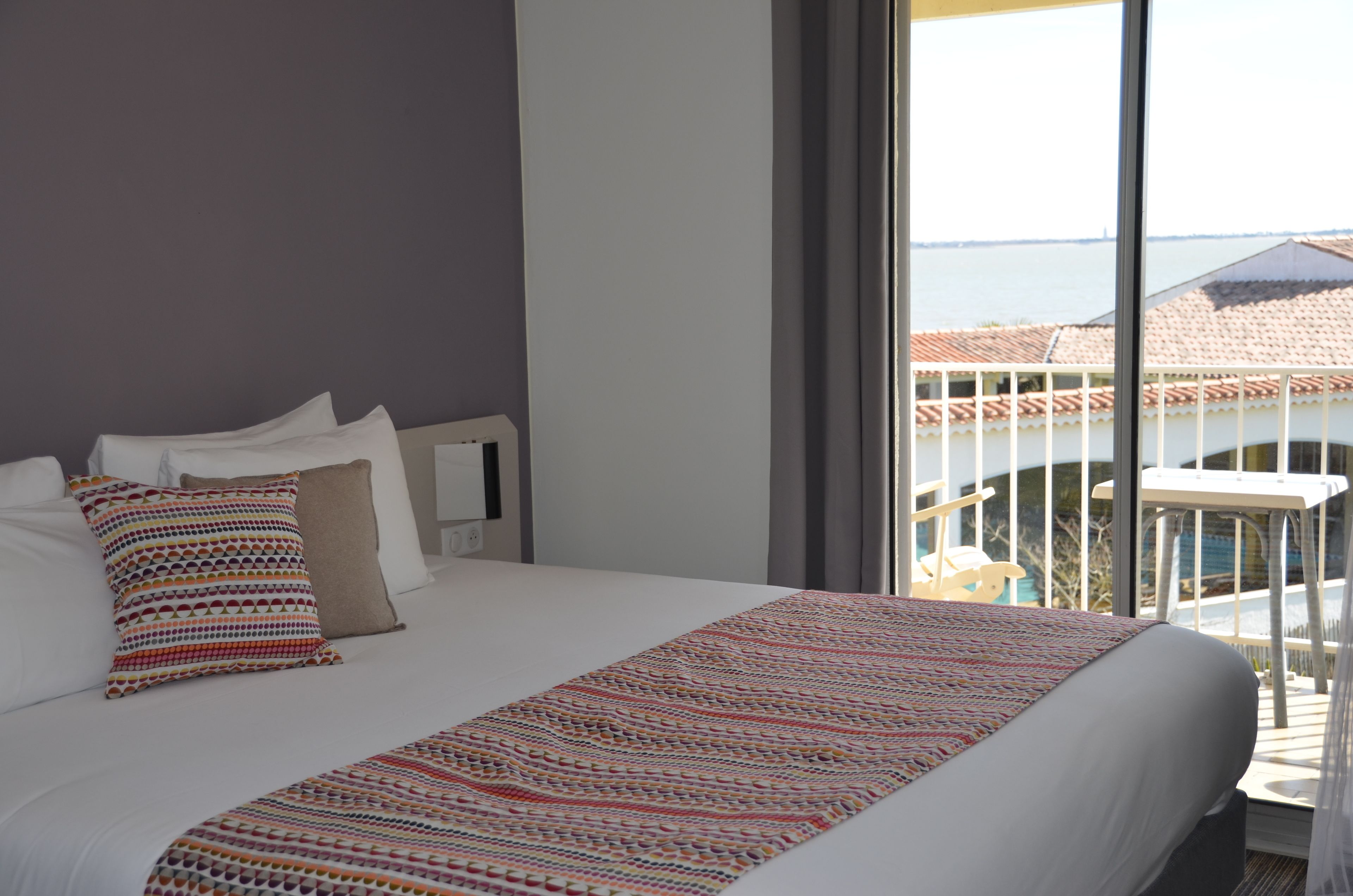 A hotel room with a large bed, a view of the sea, and a balcony with a railing.