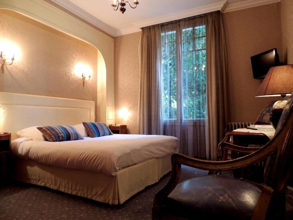 Ein Hotelzimmer mit Bett, Sessel, Fernseher und einem Fenster mit Vorhängen.