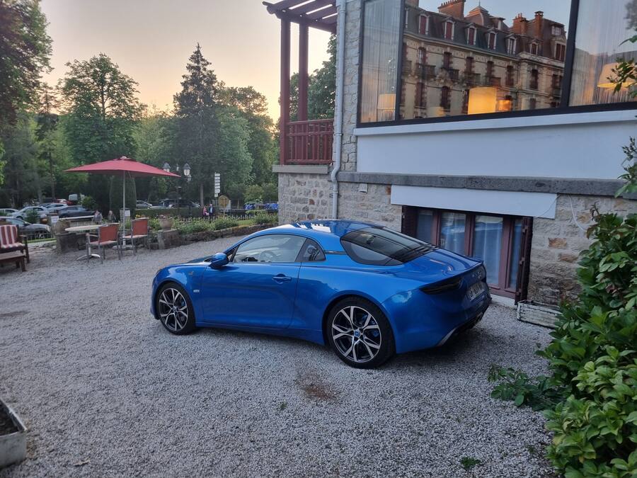 A blue sports car parked in a gravel driveway with a stone building in the background.