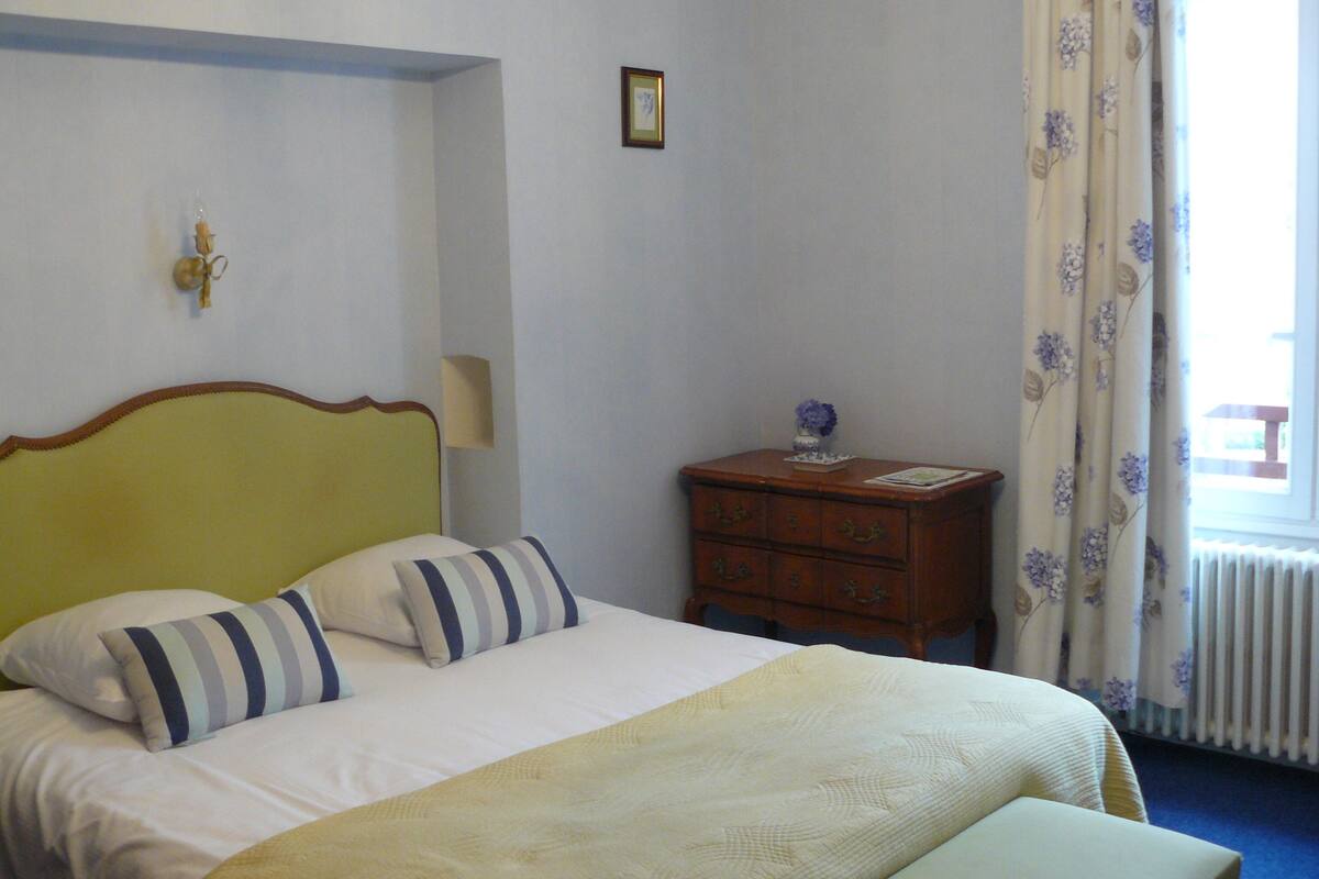Habitación de hotel con una cama, cómoda, lámpara, cuadro enmarcado en la pared y ventana con cortinas.