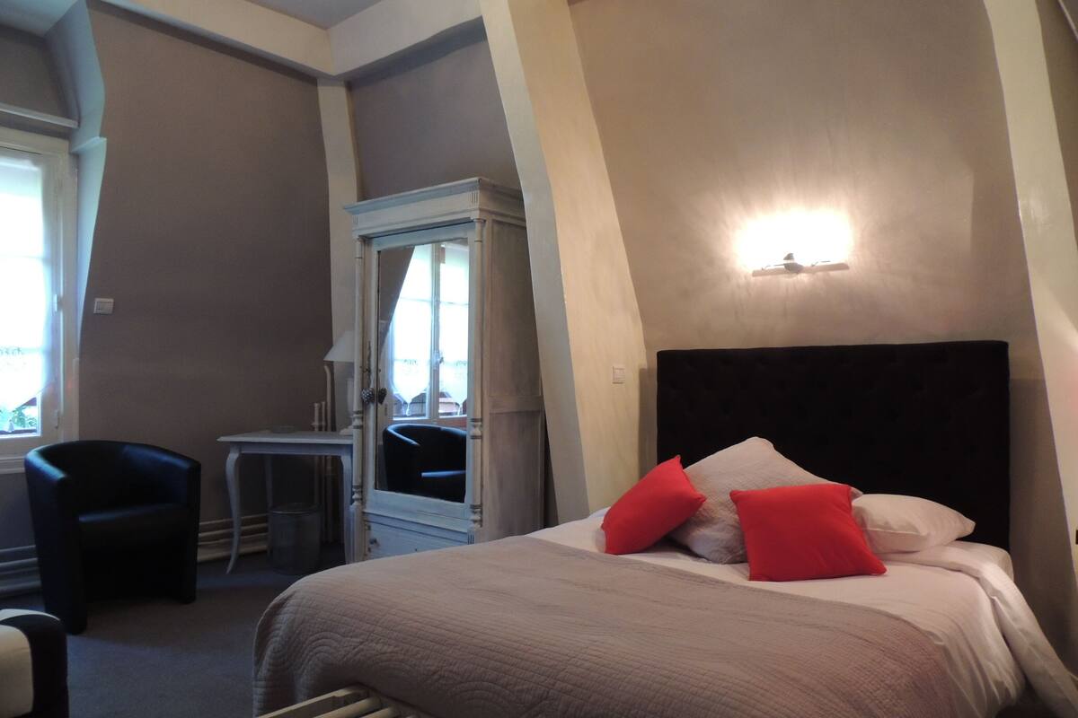 Una habitación de hotel con cama, una silla, un escritorio y un espejo.