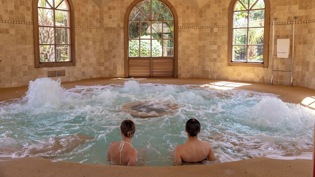 Un spa con un amplio jacuzzi, ventanas arqueadas y vistas al exterior con vegetación.