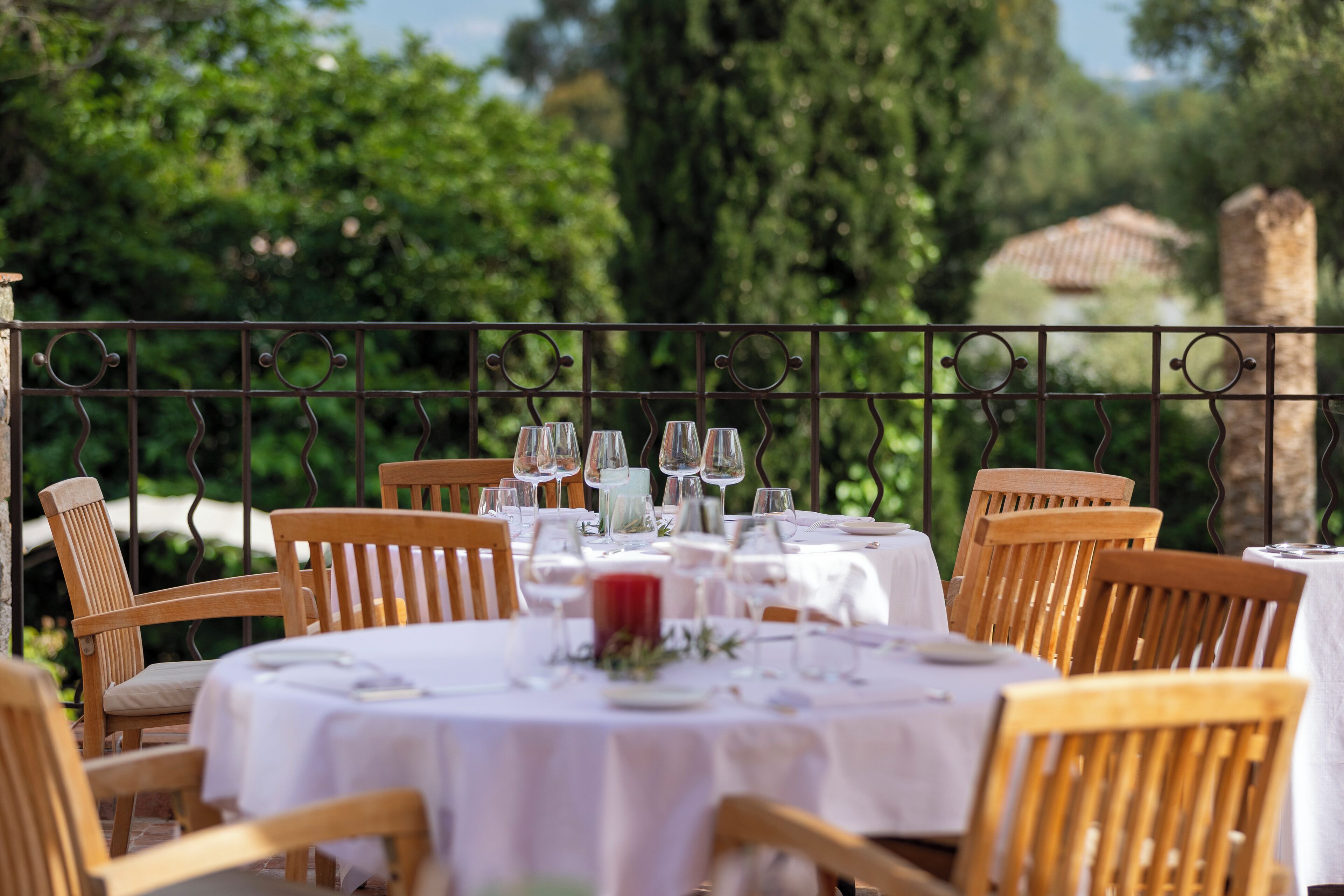 An outdoor dining area with round tables and wooden chairs, surrounded by a metal railing.