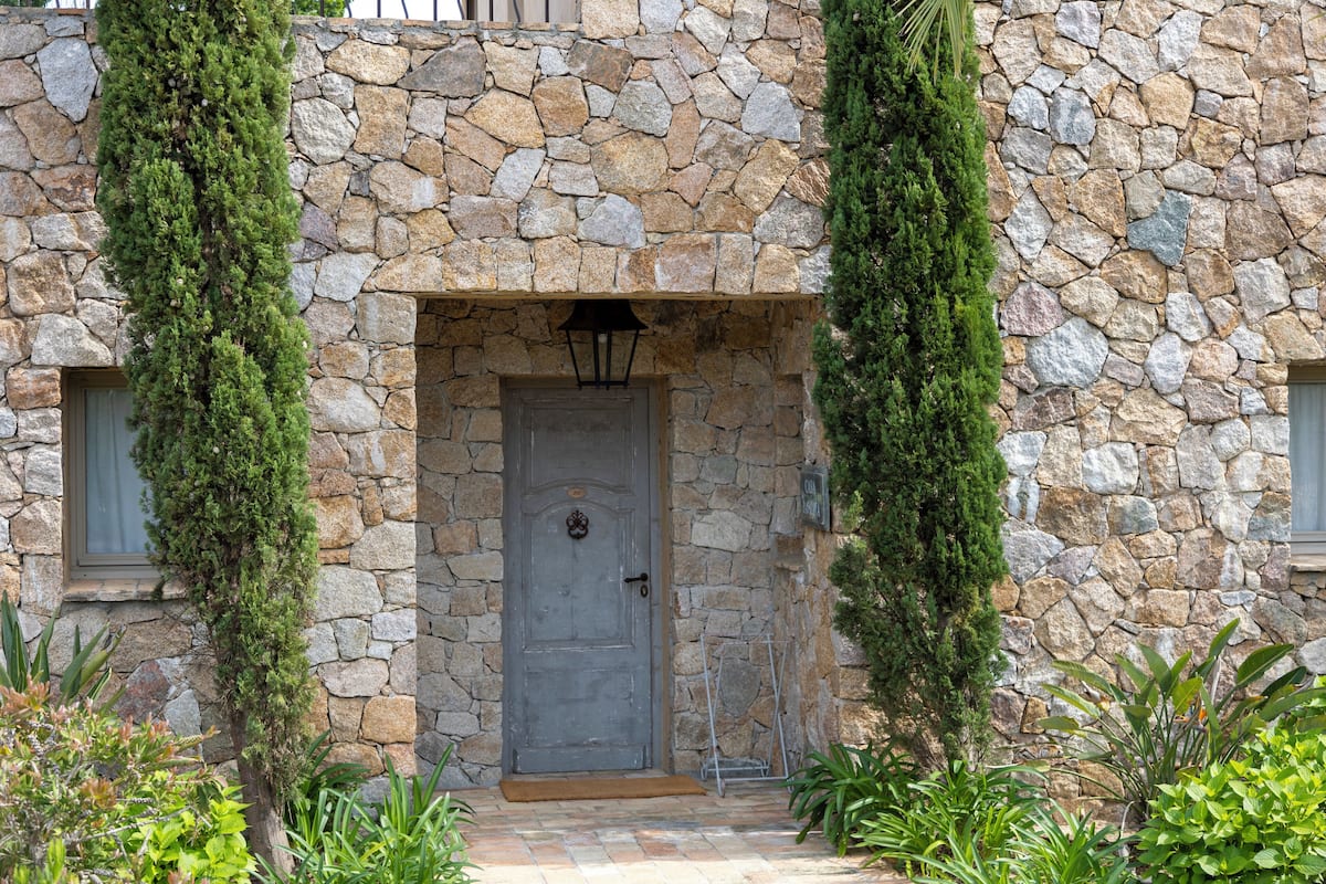 Un edificio de piedra con una puerta gris, una ventana pequeña y un farol sobre la puerta.