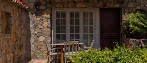 Un bâtiment en pierre doté d’une terrasse carrelée, d’une table et de chaises en bois, et d’une porte avec une fenêtre.
