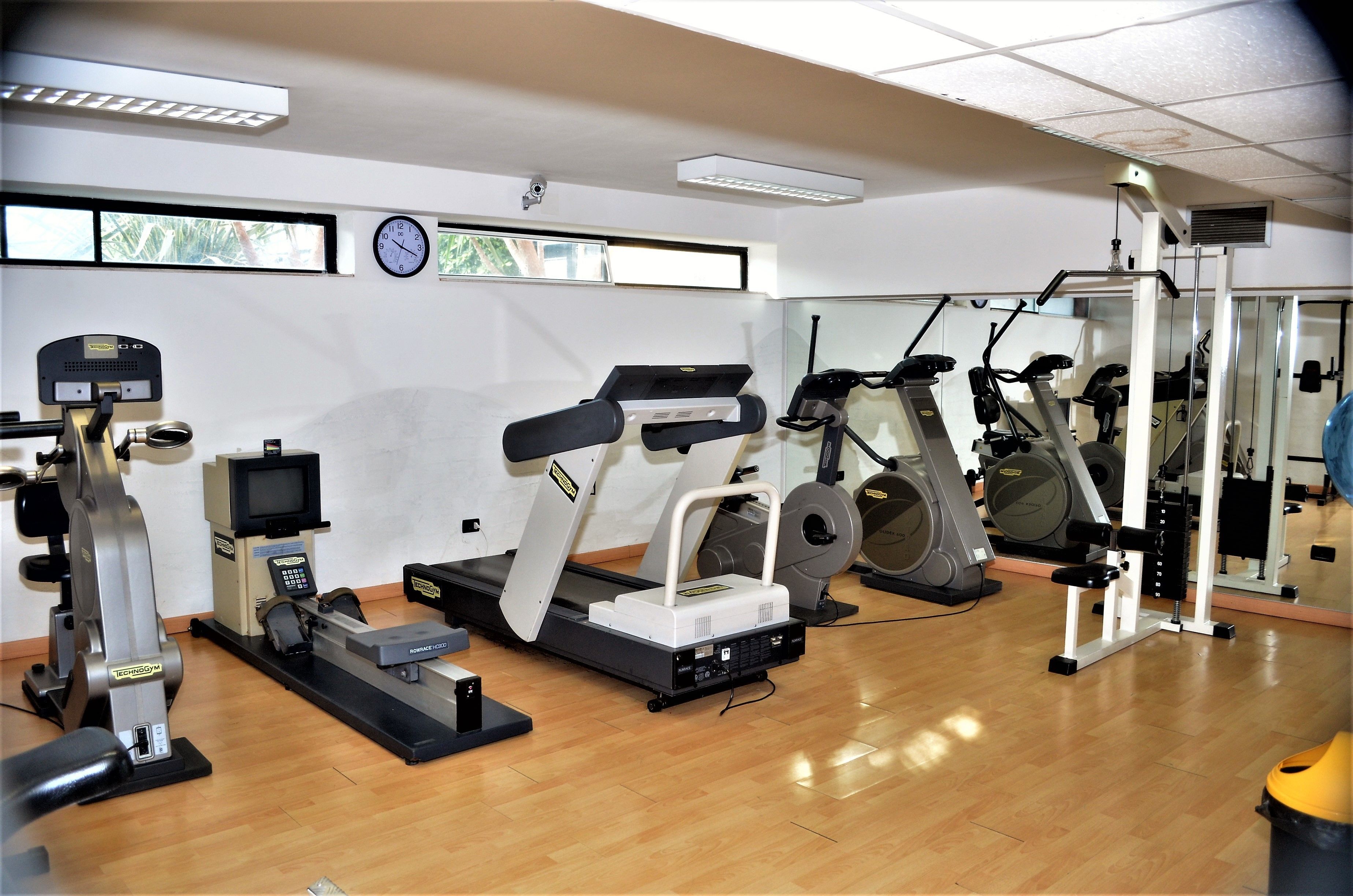 Uma academia com máquinas de cardio, um banco de musculação e um painel de espelhos.