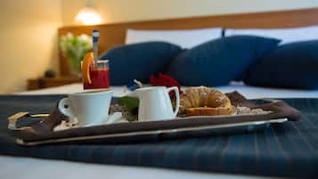 A breakfast tray with a cup of coffee, a croissant, and a glass of juice on a bed with blue bedding and a wooden headboard.