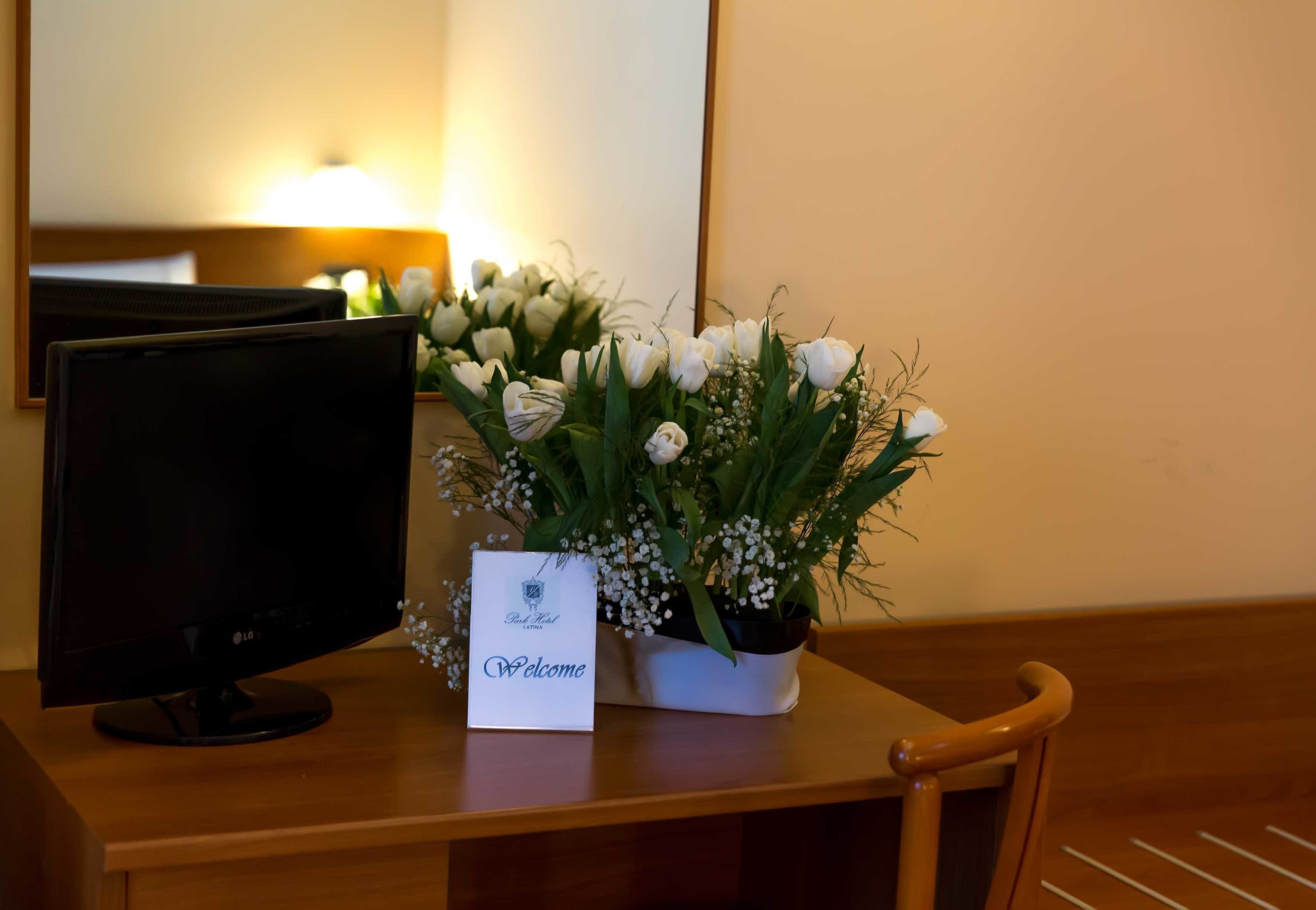 Un bureau avec un écran d’ordinateur, une carte de bienvenue et un bouquet de fleurs blanches.