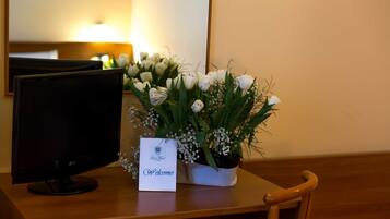 Un bureau avec un écran d’ordinateur, une carte de bienvenue et un bouquet de fleurs blanches.