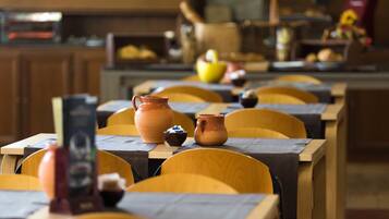 A restaurant with wooden tables and chairs, some with placemats and a few with a small bowl and a pitcher.
