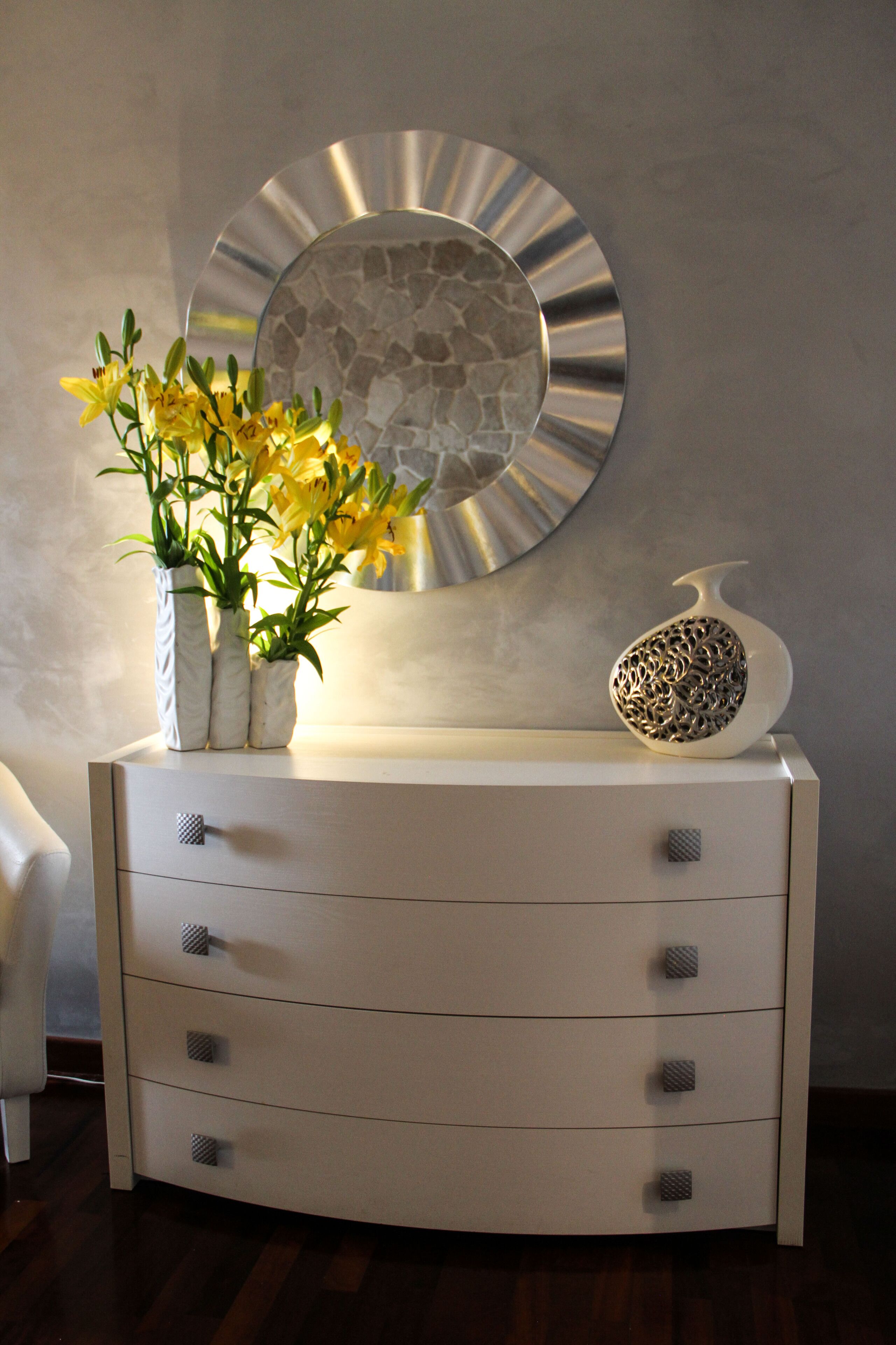 Une commode blanche à trois tiroirs, sur laquelle est posé un vase rempli de fleurs jaunes.
