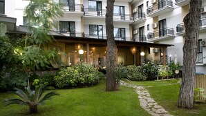 Un patio con sendero de piedra, abundante vegetación y un edificio con varios balcones y ventanas.
