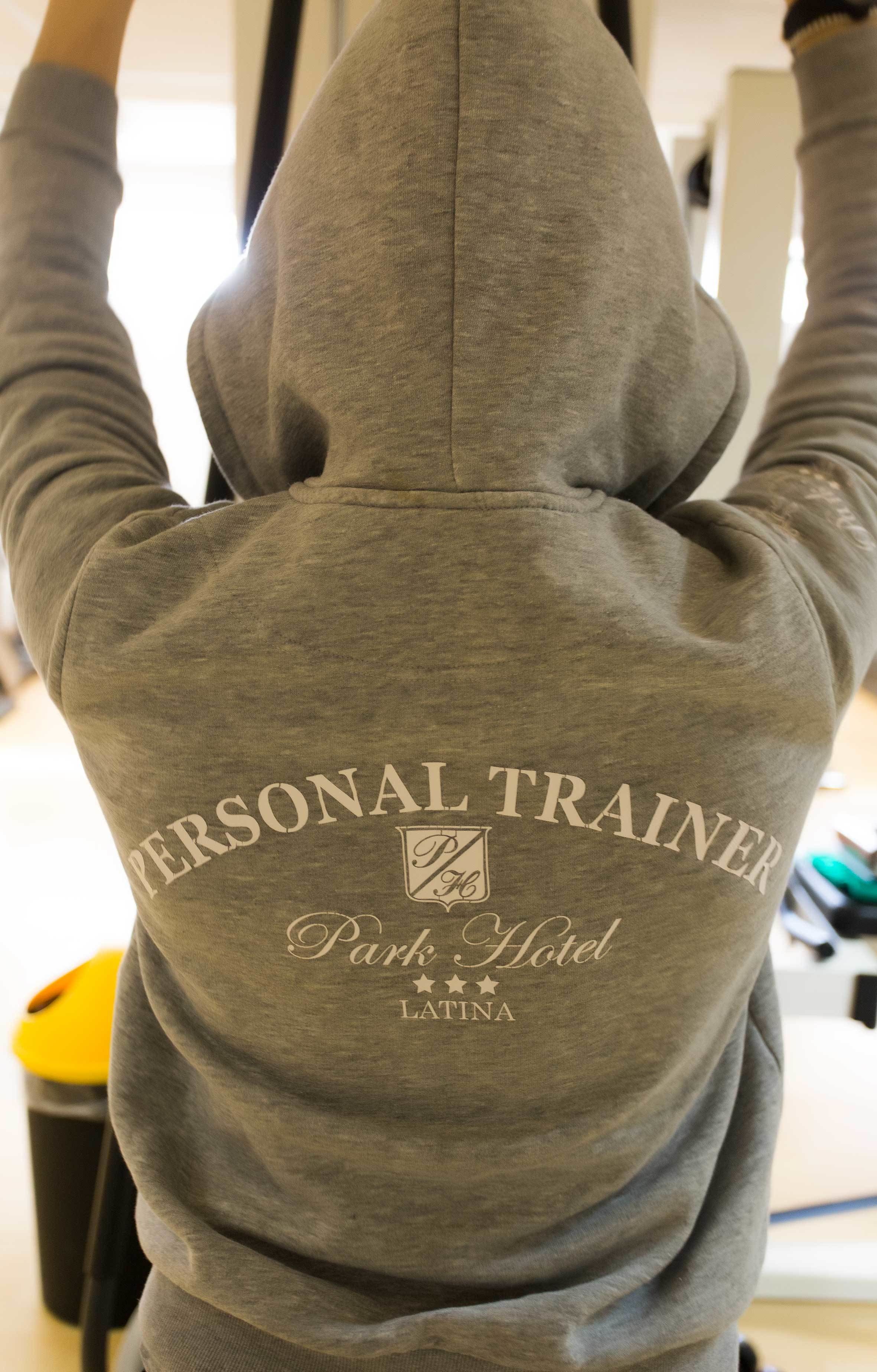 Eine graue Kapuzenjacke mit dem Aufdruck 'PERSONAL TRAINER Park Hotel LATINA' auf dem Rücken.