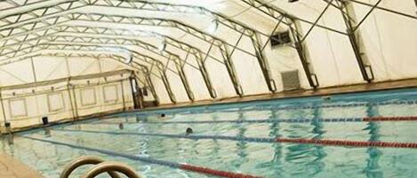 Una piscina techada con carriles delimitados y una estructura de techo metálica.