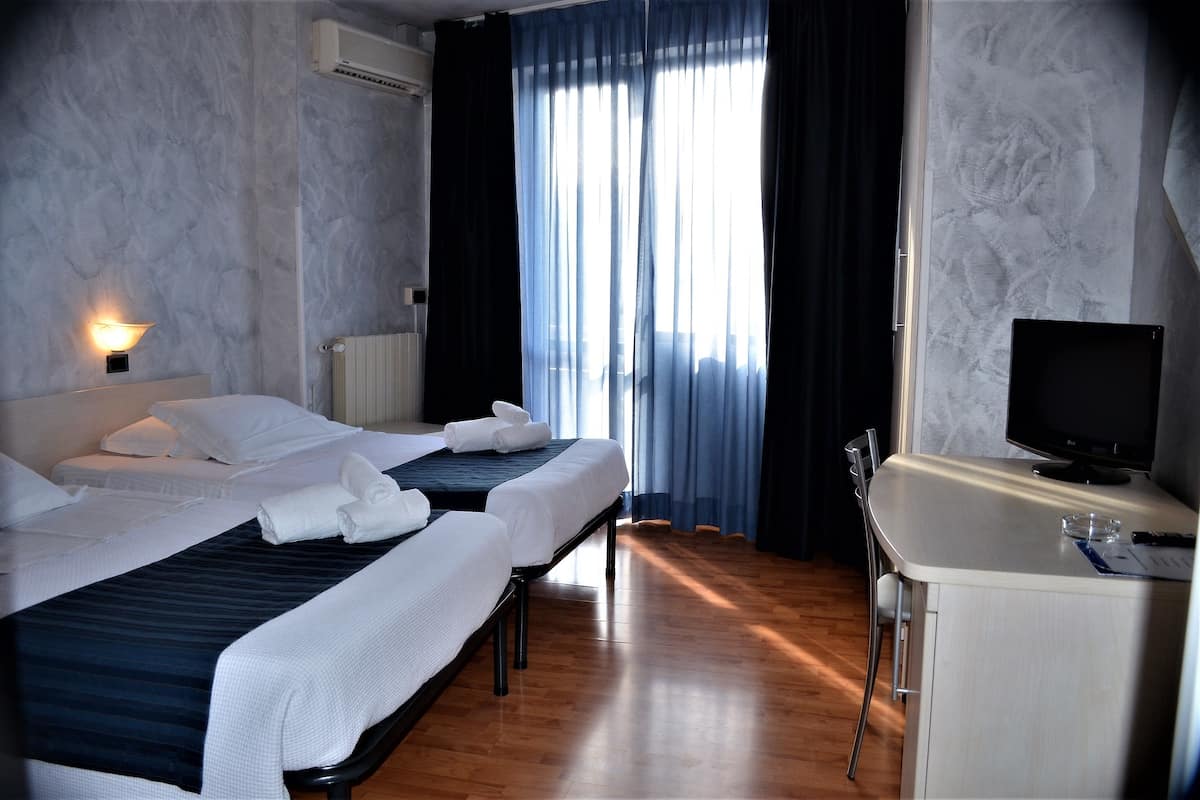 Une chambre d’hôtel avec deux lits, un bureau avec un ordinateur et une fenêtre avec des rideaux.