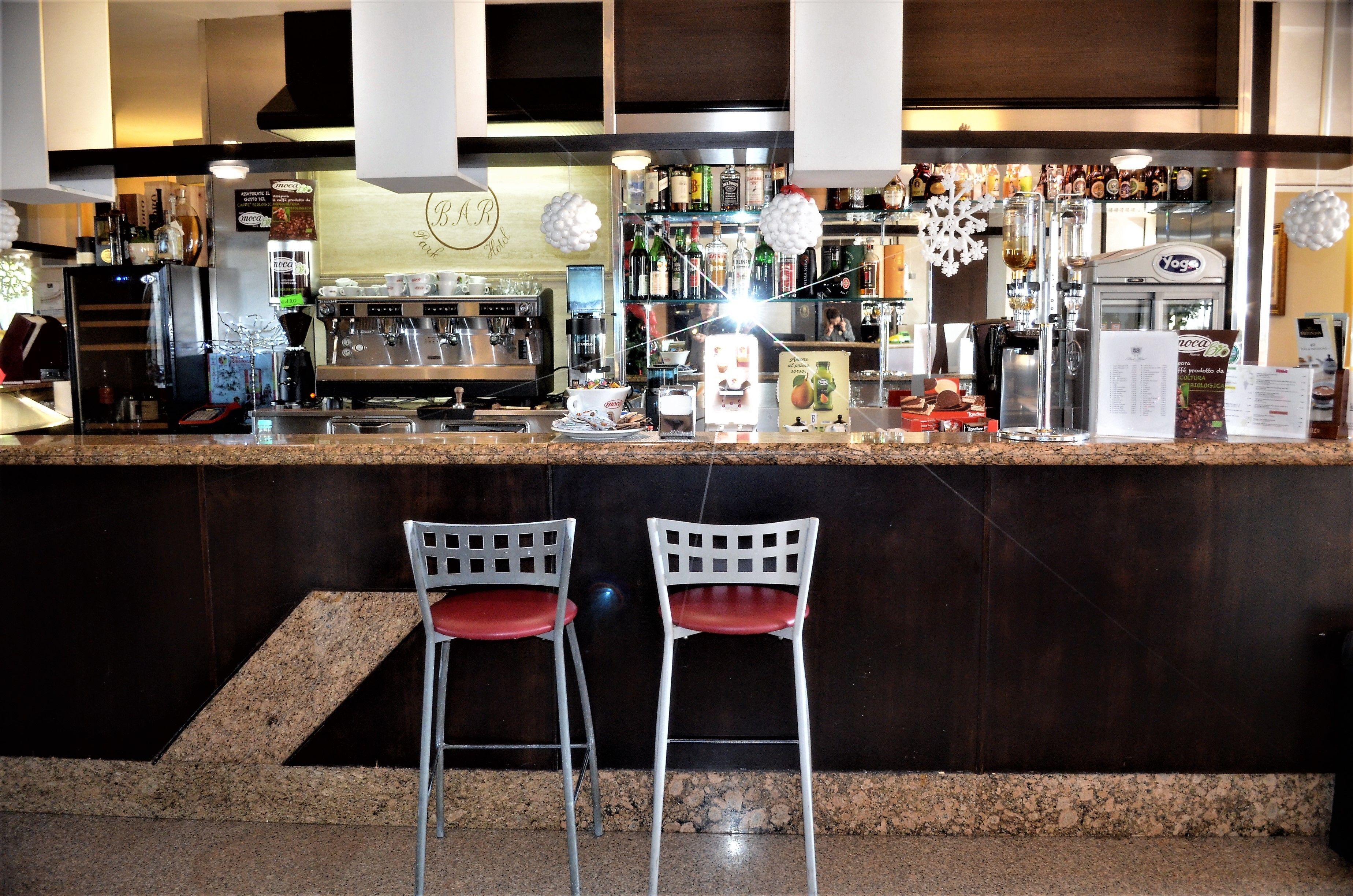 A bar area with two white chairs, a counter with various bottles and a coffee machine, and a sign for 'B.A.R.'