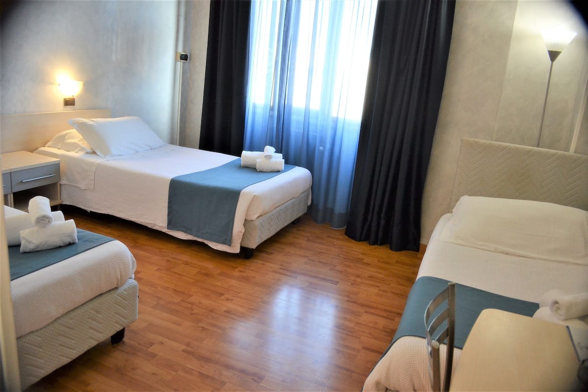 Une chambre d’hôtel avec deux lits, une table de chevet, une lampe et une fenêtre avec des rideaux.
