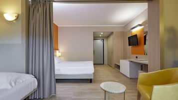 Habitación de hotel con una cama, una mesita redonda pequeña, una silla amarilla, un escritorio con televisor de pantalla plana y un baño visible a través de una puerta abierta.