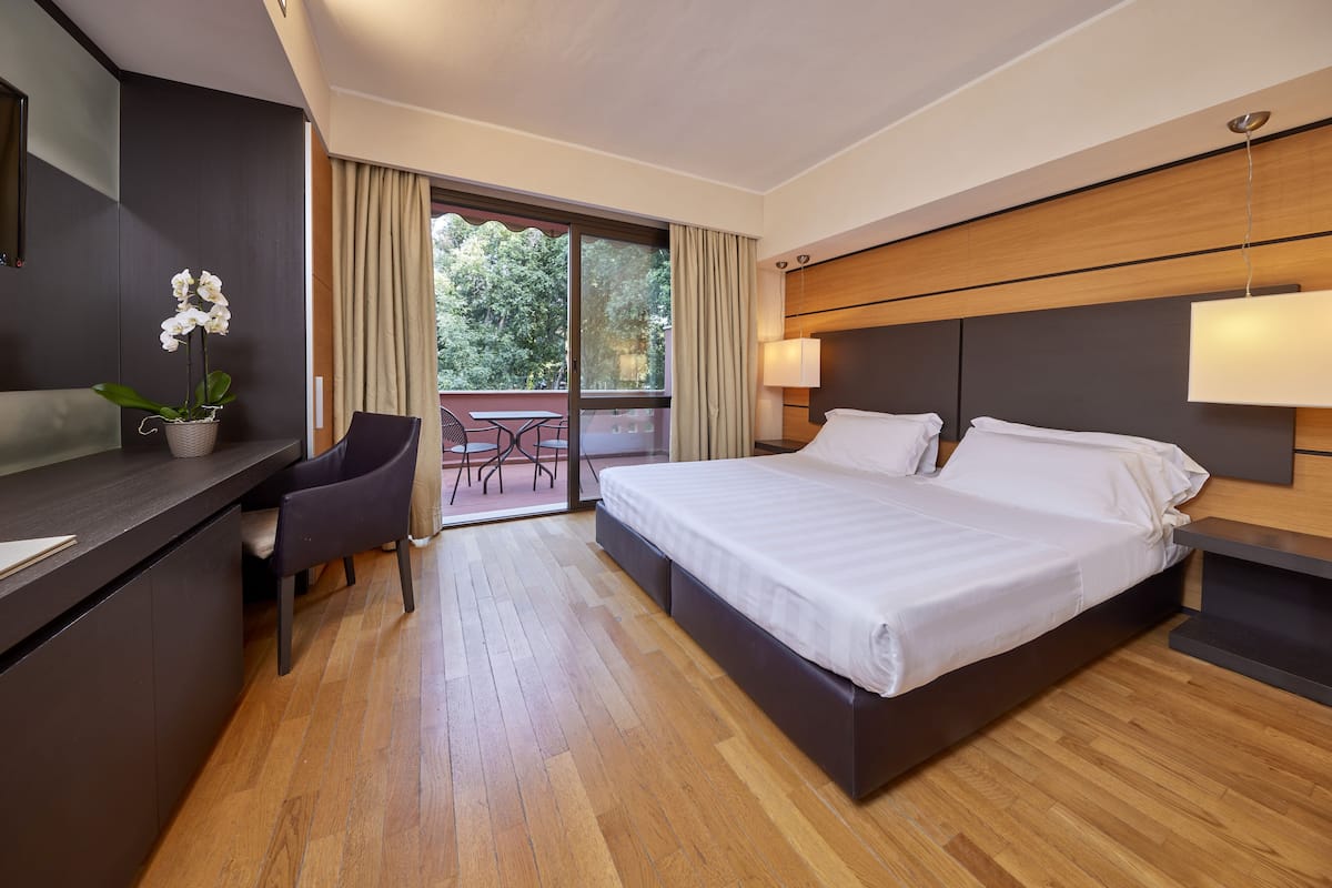 Una habitación de hotel moderna con una cama grande, un escritorio, una silla y un balcón con vistas a árboles.