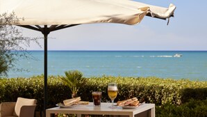 Ein Essplatz im Freien mit Blick auf das Meer, ein Bierglas und Sandwiches.