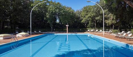 A clear blue swimming pool with a tiled deck, surrounded by lounge chairs and trees.