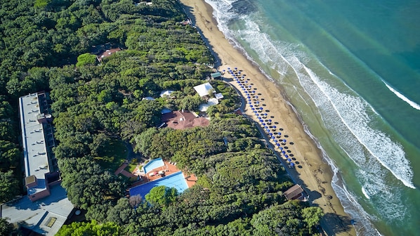 Luchtbeeld van een kustbezit met een strand, een parkeerplaats en een gebouw met een blauw dak.