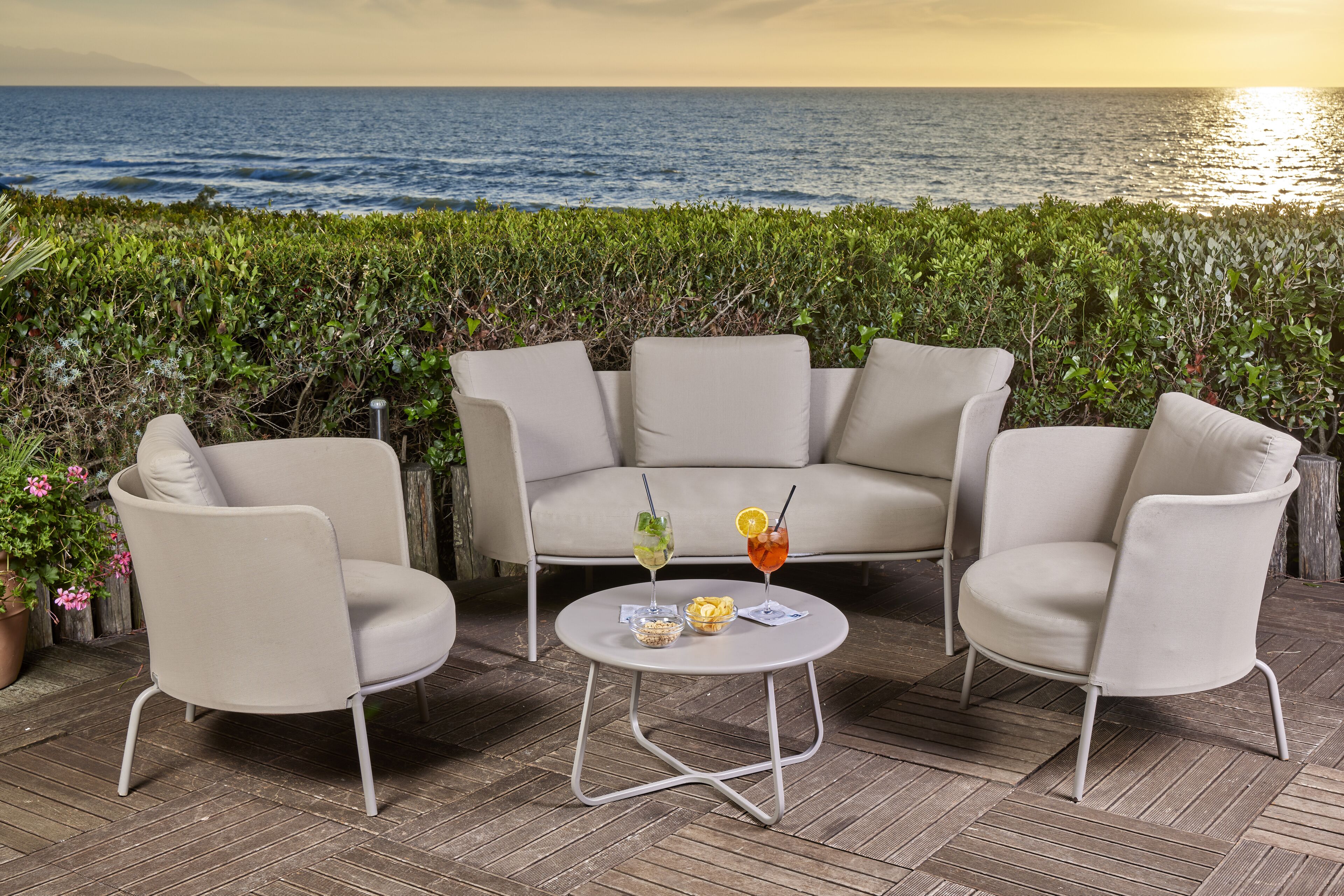 Eine Terrasse mit einer beigefarbenen Sofagarnitur, einem kleinen runden Tisch und zwei Getränken.
