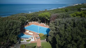 Eine Luftaufnahme eines Resorts mit einem Swimmingpool, umgeben von Liegestühlen, vor einer Kulisse aus üppiger Vegetation und dem Meer.