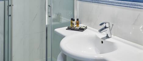 Un baño moderno con ducha envuelta en vidrio, un lavabo blanco y un espejo encima.