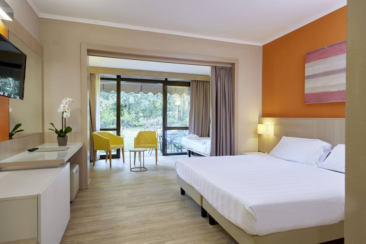 Una habitación de hotel con cama, escritorio, silla, mesita y ventana con cortinas.