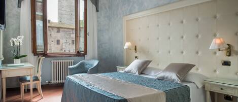 Un dormitorio con una cama grande, un escritorio, una silla y una ventana con vistas a edificios.